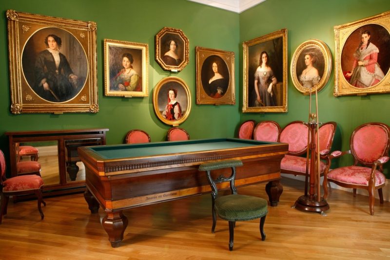 Sala interior del Museo del Romanticismo con varios retratos colgados y una mesa de billar