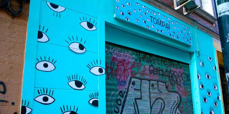 Pared azul de un local con ojos pintados y un graffiti en la puerta