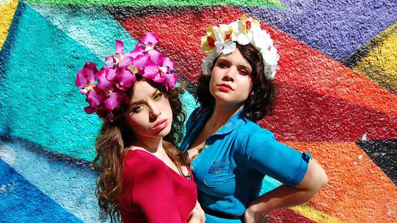 Las actrices posando con flores en la cabeza en una pared de colores