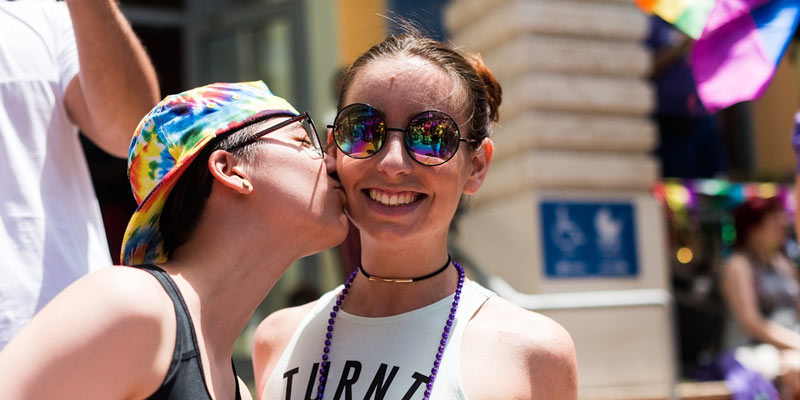dos chicas en el Orgullo. Una besa en la mejilla a otra.