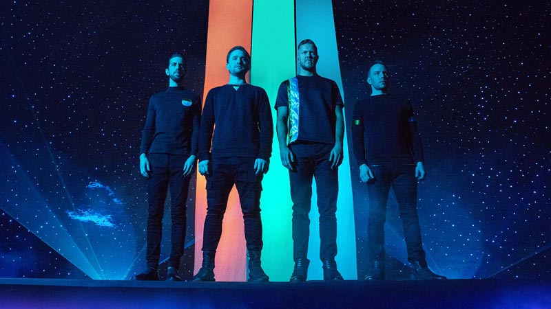 el grupo de imagine dragons vestidos de negro con un fondo estrellado detrás