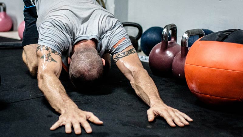 hombre arrodillado, estirando, y varias pesas de distintos tamaños a su lado
