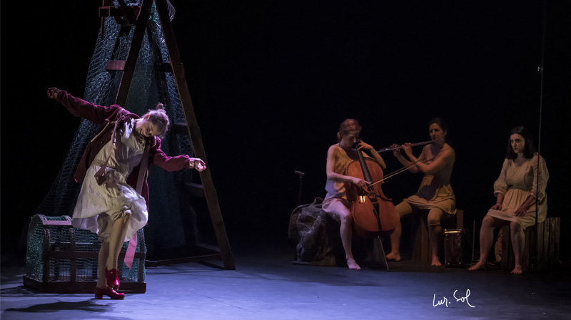 Mientras una mujer baila otras tres tocan unos instrumentos. 