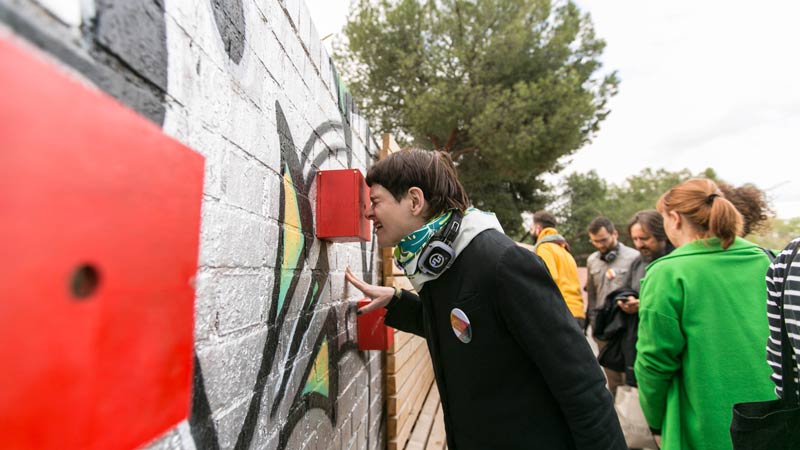 Una mujer mira a través de un agujero de una caja roja en medio de una intervención artística