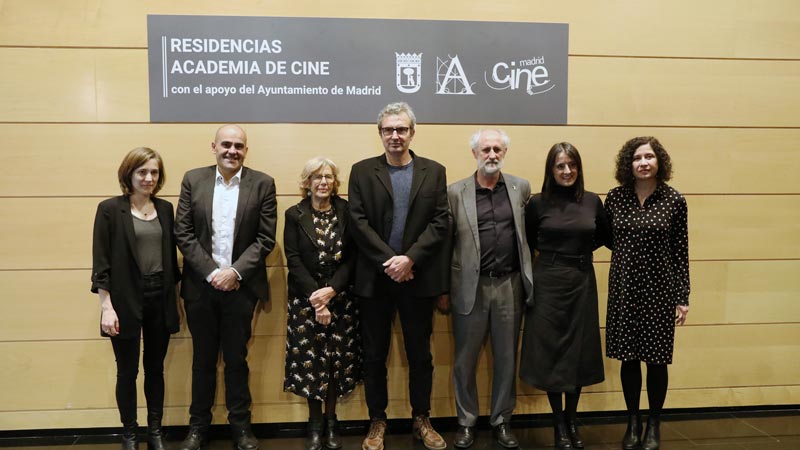 Mariano Barroso, la alcaldesa Manuela Carmena, Belén Atienza (productora), Carla Simón (directora y guionista) y la coordinadora de Ciudad de Madrid Film Office, Ángeles Vacas,posando en la presentación de la convocatoria junto al cartel de las Residencias de la Academia de Cine