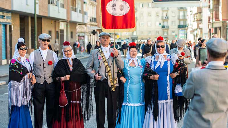 Grupo de gente mayor vestidos de chulapas y chulapos en medio de la calle haciéndose una foto con un móvil