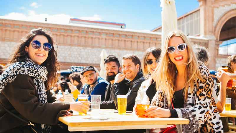 Grupo de amigos comiendo y bebiendo en las mesas junto a los food trucks