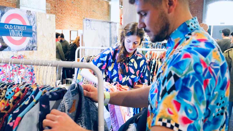 Un chico y una chica colocando ropa en un puesto vintage