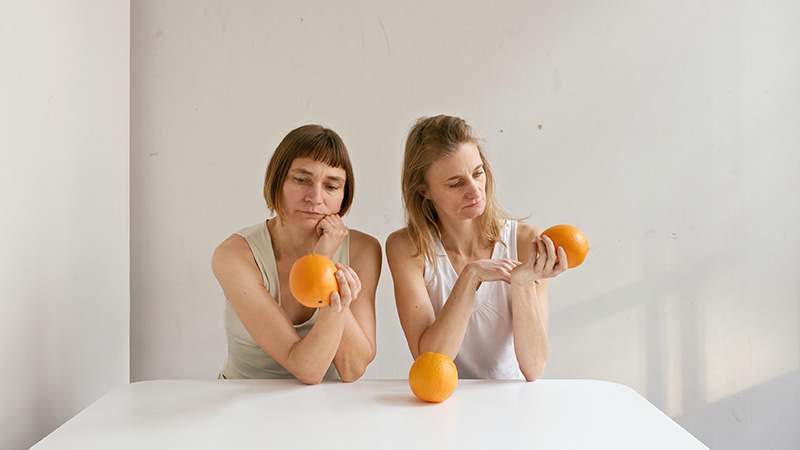 Obra de Elina Brotherus donde pueden verse a dos mujeres mirando tres naranjas sobre un fondo blanco