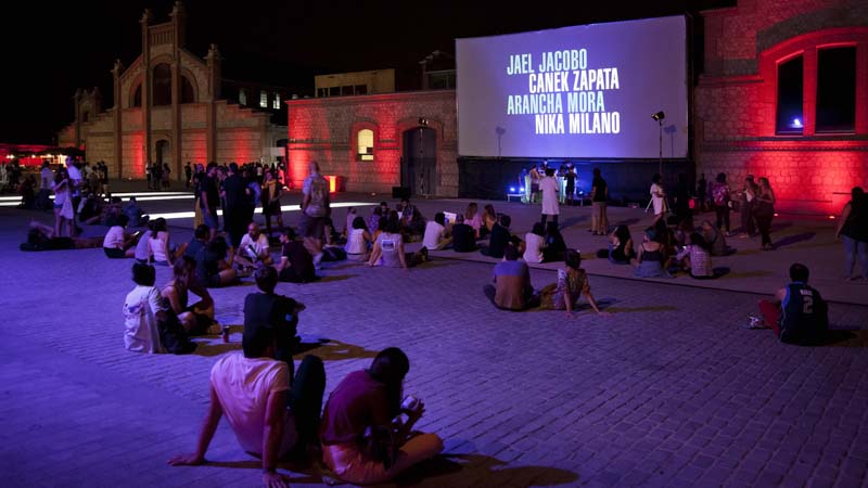 Gente sentada en un patio de Matadero disfrutando de los cortometrajes de la 1ª edición de ANIMARIO